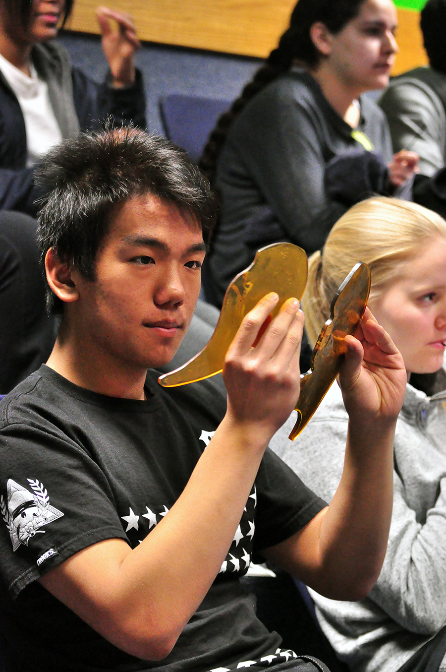 Teenaged asian boy looks at diagram of lungs as he attempts to breathe through a straw to simulate smokers lungs.