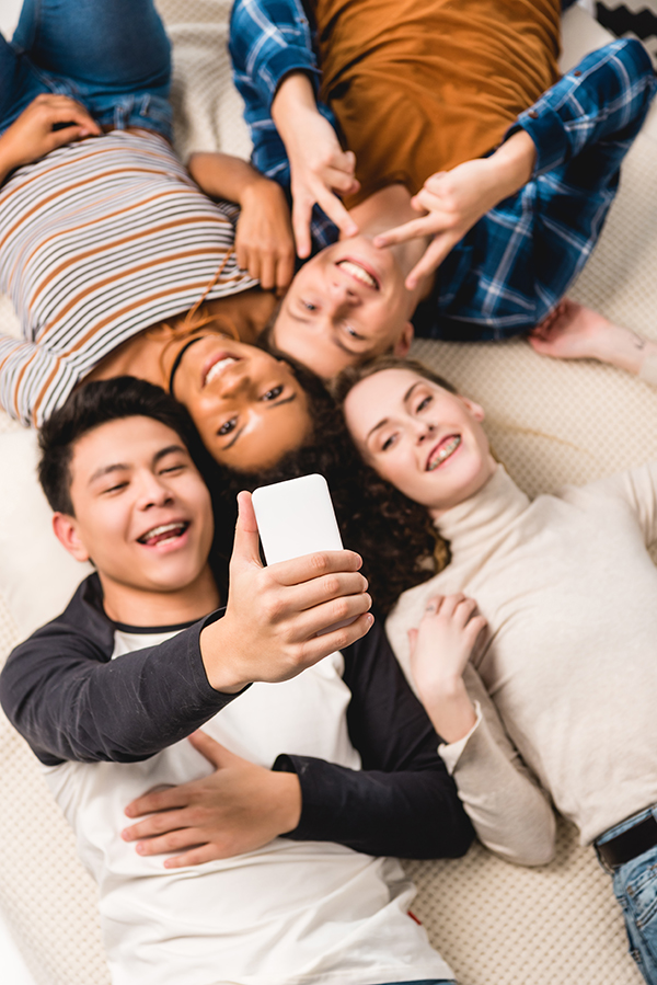 Four teens lay on the ground taking a selfie.