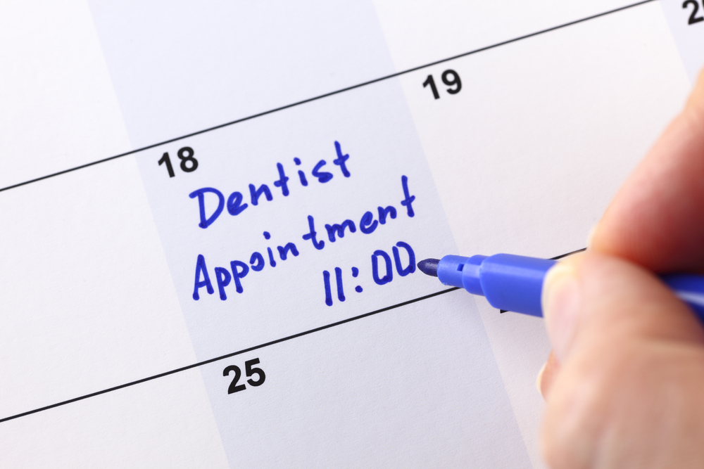 Human hand writes reminder "Dentist appointment 11:00" in calendar.