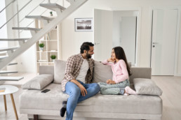 Happy young indian father with teenage child daughter having fun enjoying talking spending time at home. Smiling dad and teen kid girl having conversation sitting on sofa in modern house living room.