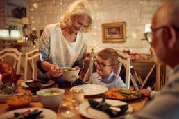 Happy senior woman serving food to her grandson during Thanksgiving meal at dining table.