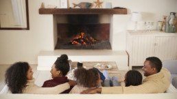 Family Sitting On Sofa In Lounge Next To Open Fire