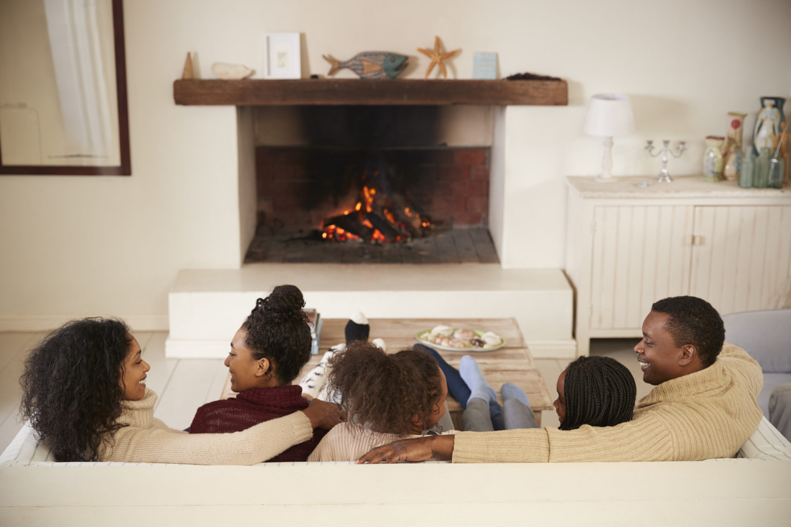 Family Sitting On Sofa In Lounge Next To Open Fire