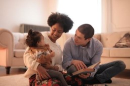 Two adults and a baby looking at an open book in a living room