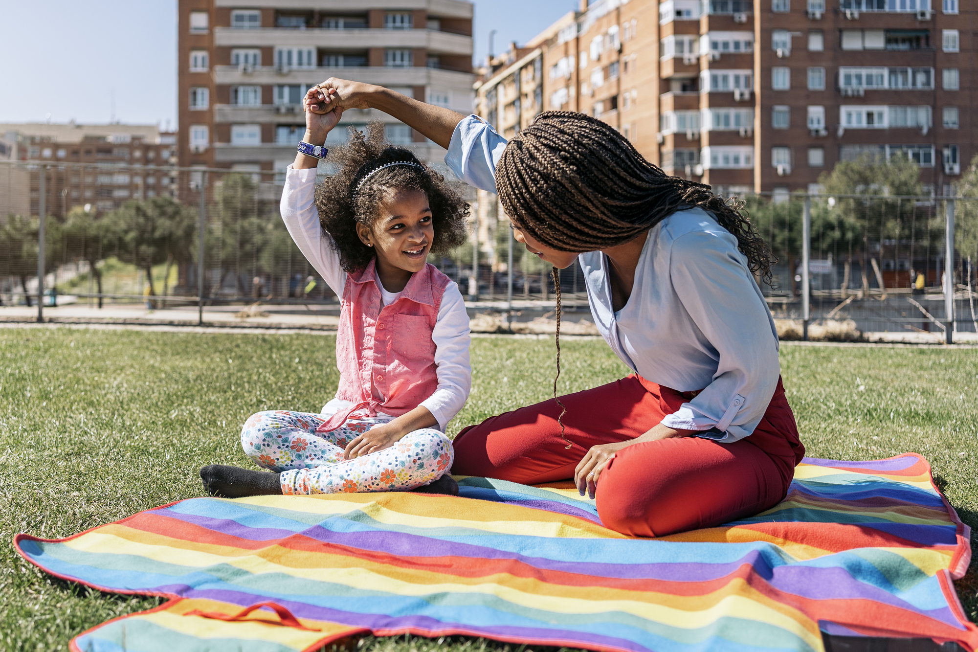 Beautiful African American girl sitting in the grass with her mother. They are playing and enjoying sunny day.