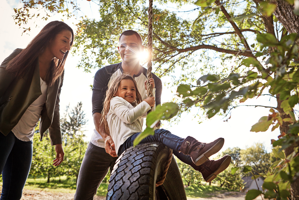 A happy mother and father pushing their daughter on a tire swing