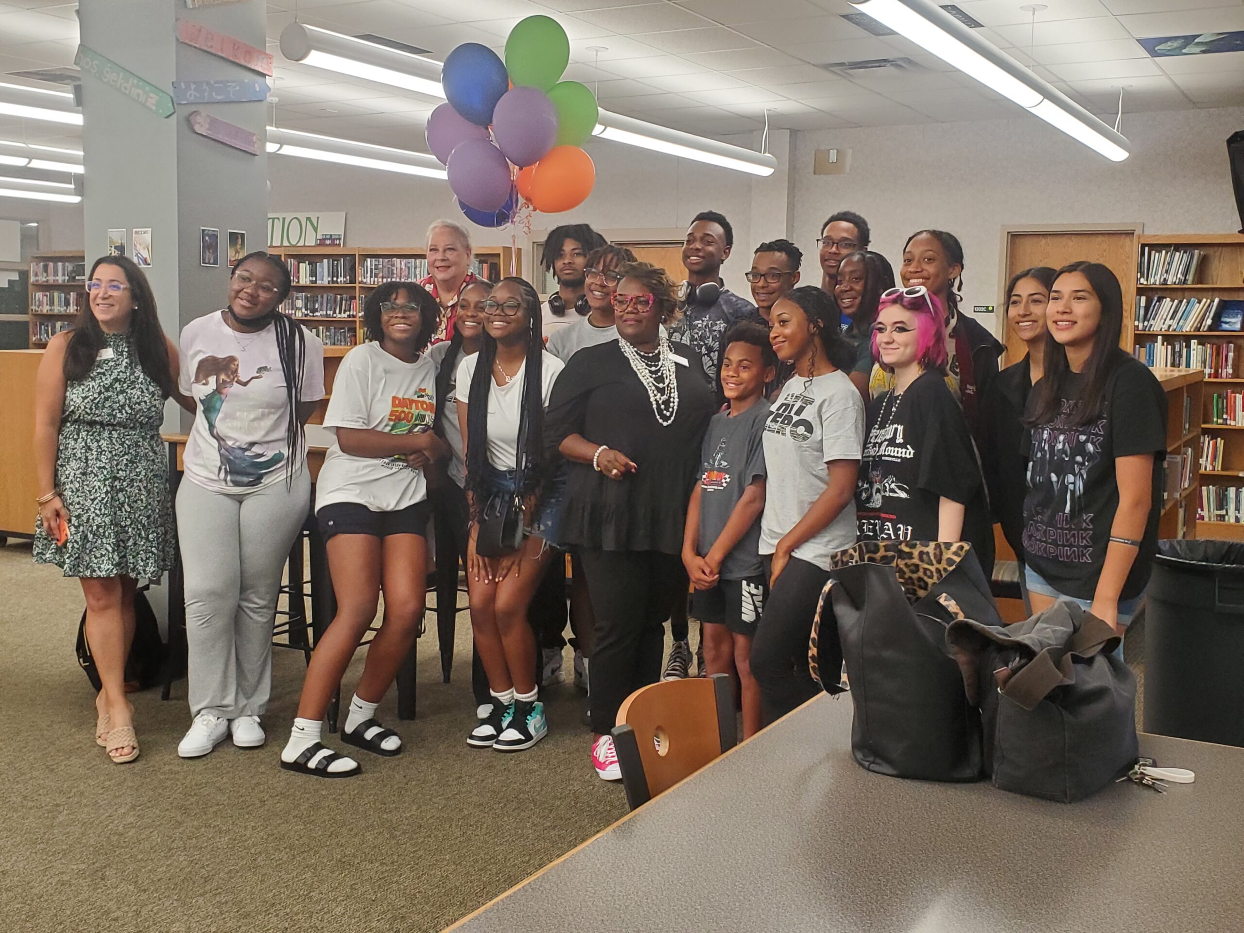 Shaconda Jarman of Enloe High School receiving her award surrounded by her students, inside a library, with the Poe Center's Executive Director Ann.