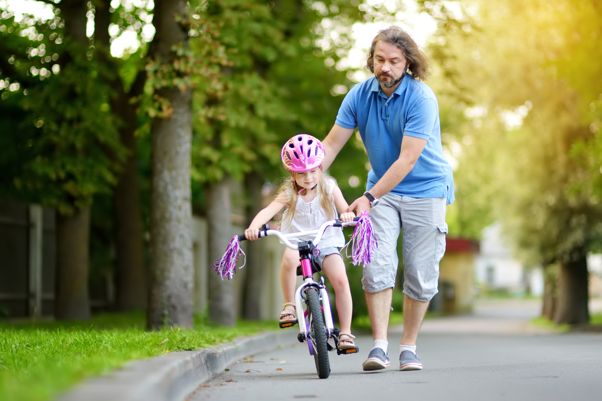 Happy father teaching his little daughter to ride a bicycle. Child learning to ride a bike. Family activities at summer.