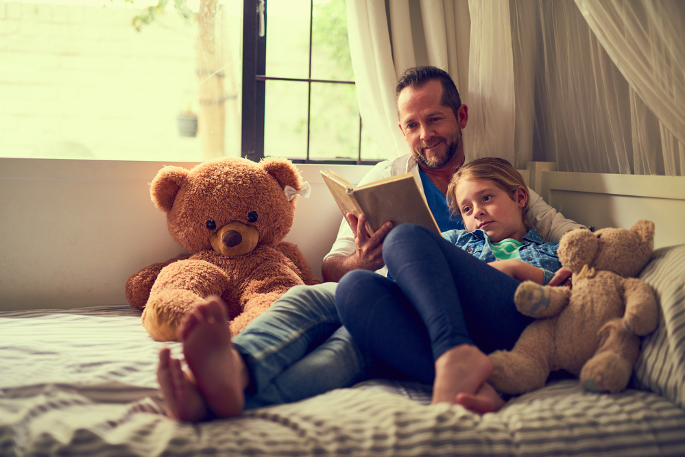 Shot of a father reading a story to his little daughter at home.