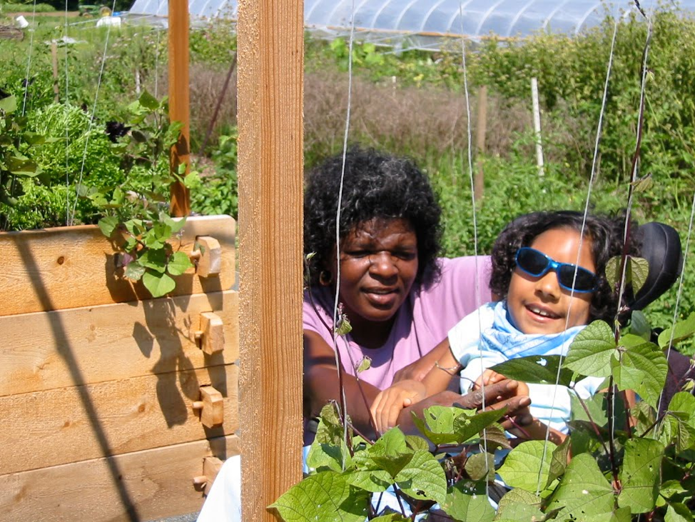 Woman helping a child see a plant in a garden.