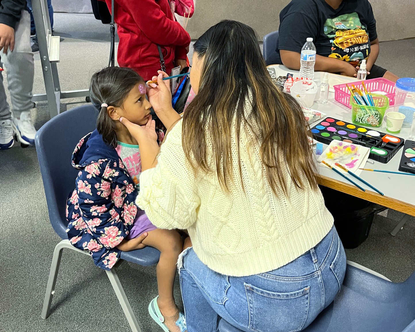 Young participants of the Summer Meals program at the Poe Center smile at the camera as they eat nutritious lunches outside on a picnic table.