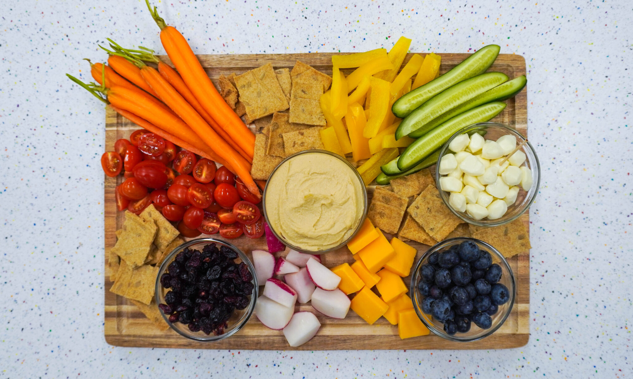 A wooden board covered in various vegetables and seeded crackers.