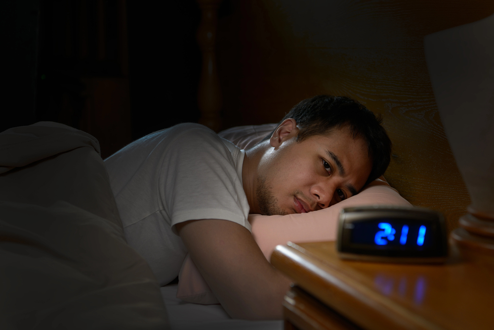Sleepless teenager lying in bed stares at digital alarm clock on desk.