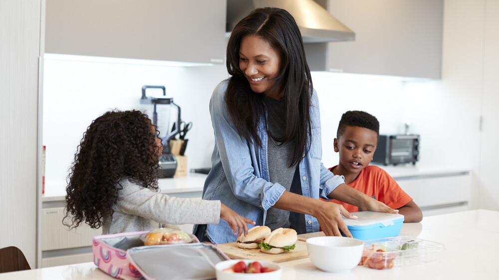 Children In Kitchen At Home Helping Mother To Make Healthy Packed Lunch