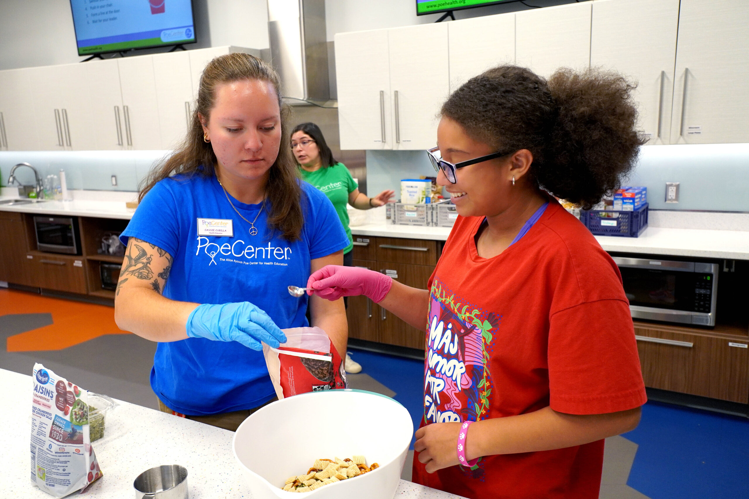 A camper measures food with the help of a camp counselor at the Poe Center CookWELL Kitchen at the Poe Center.
