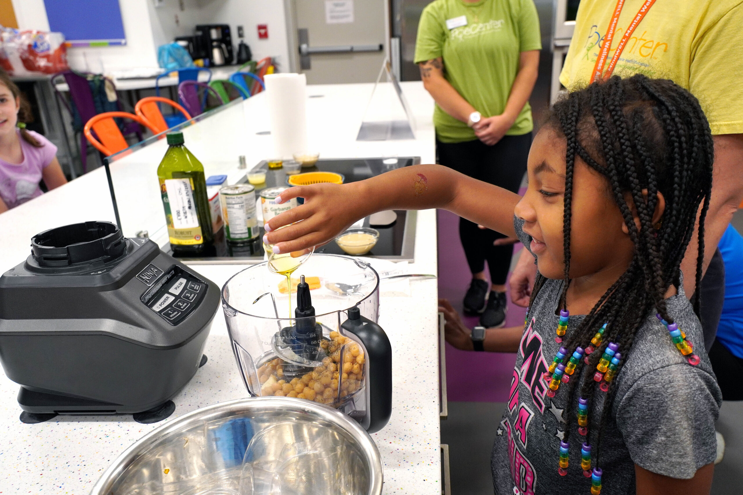 A camper measures food with the help of a camp counselor at the Poe Center CookWELL Kitchen at the Poe Center.