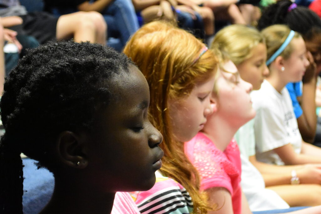 Youth practice mindfulness in an auditorium their eyes closed