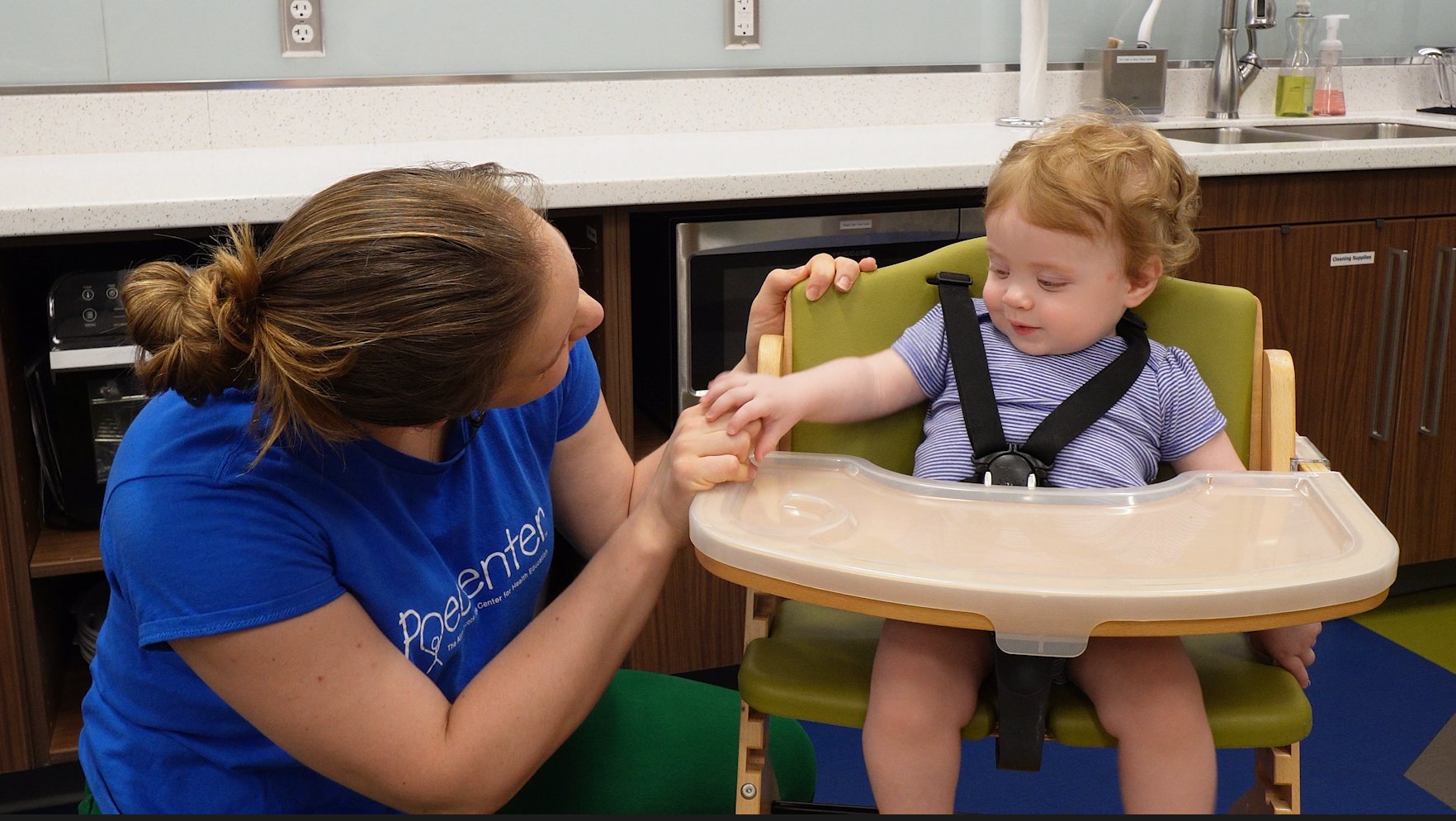 Health educator and mother talks to her child in their feeding chair.