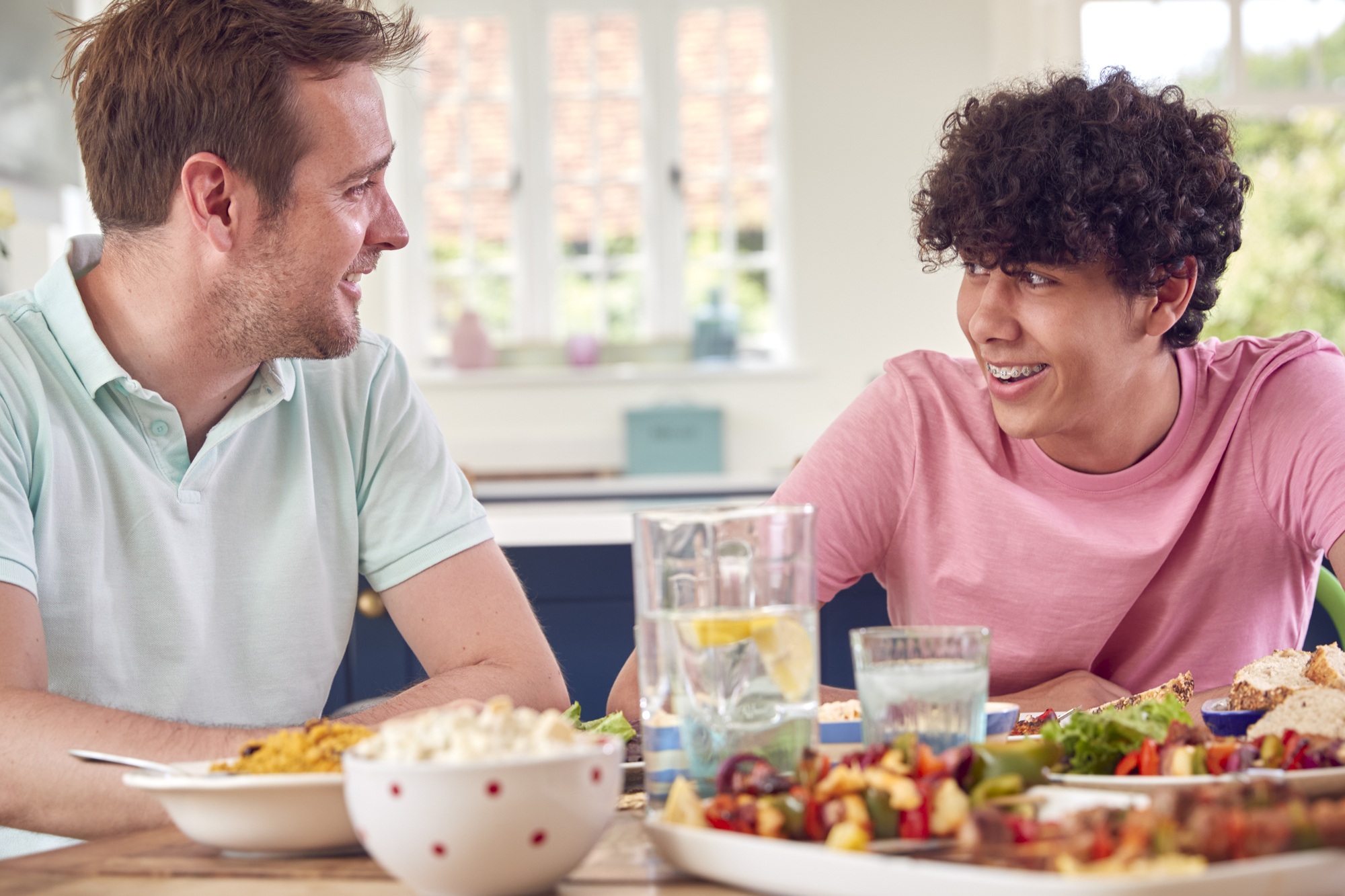 An adult and teenaged child have a conversation while eating dinner in their home
