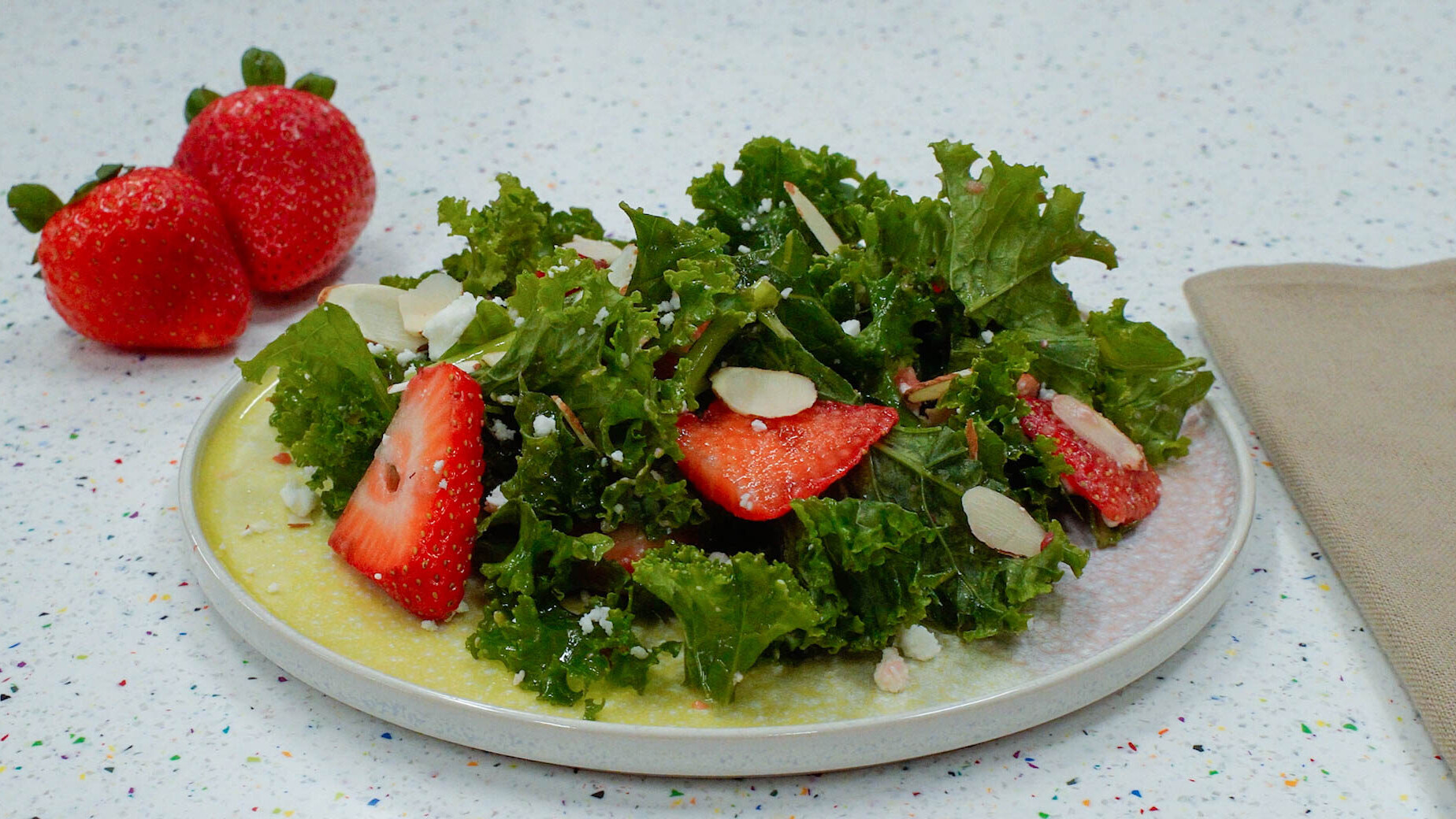 Strawberry Kale Salad topped with sliced strawberries, almonds, and feta.