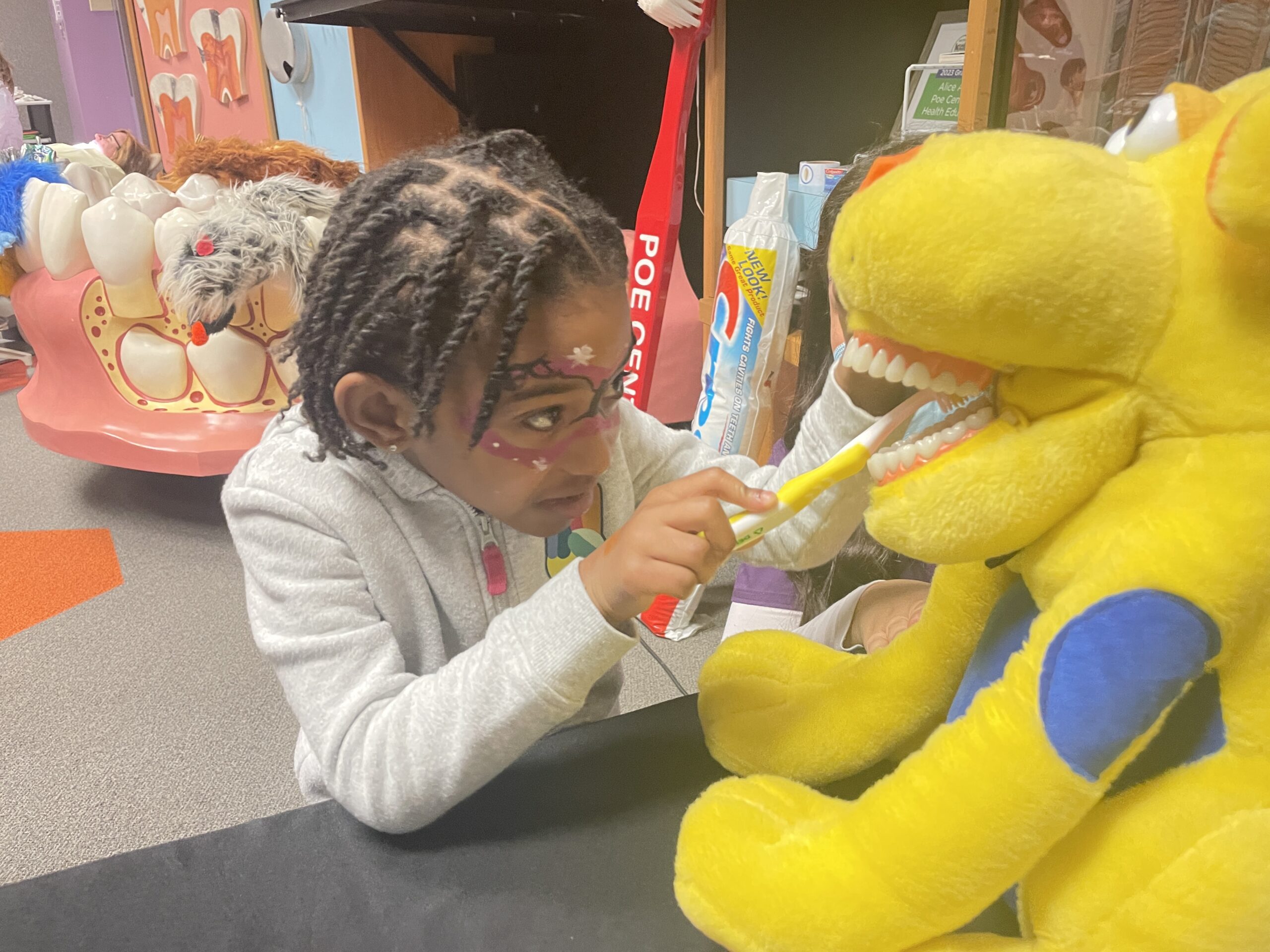 A child brushes the teeth of a yellow stuffed dinosaur toy during Terrific Teeth Day 2025