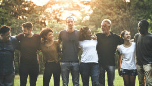 Group of adults and young people standing with linked arms, talking and laughing