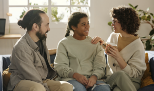 Two parents sit on a couch talking with their teenaged daughter