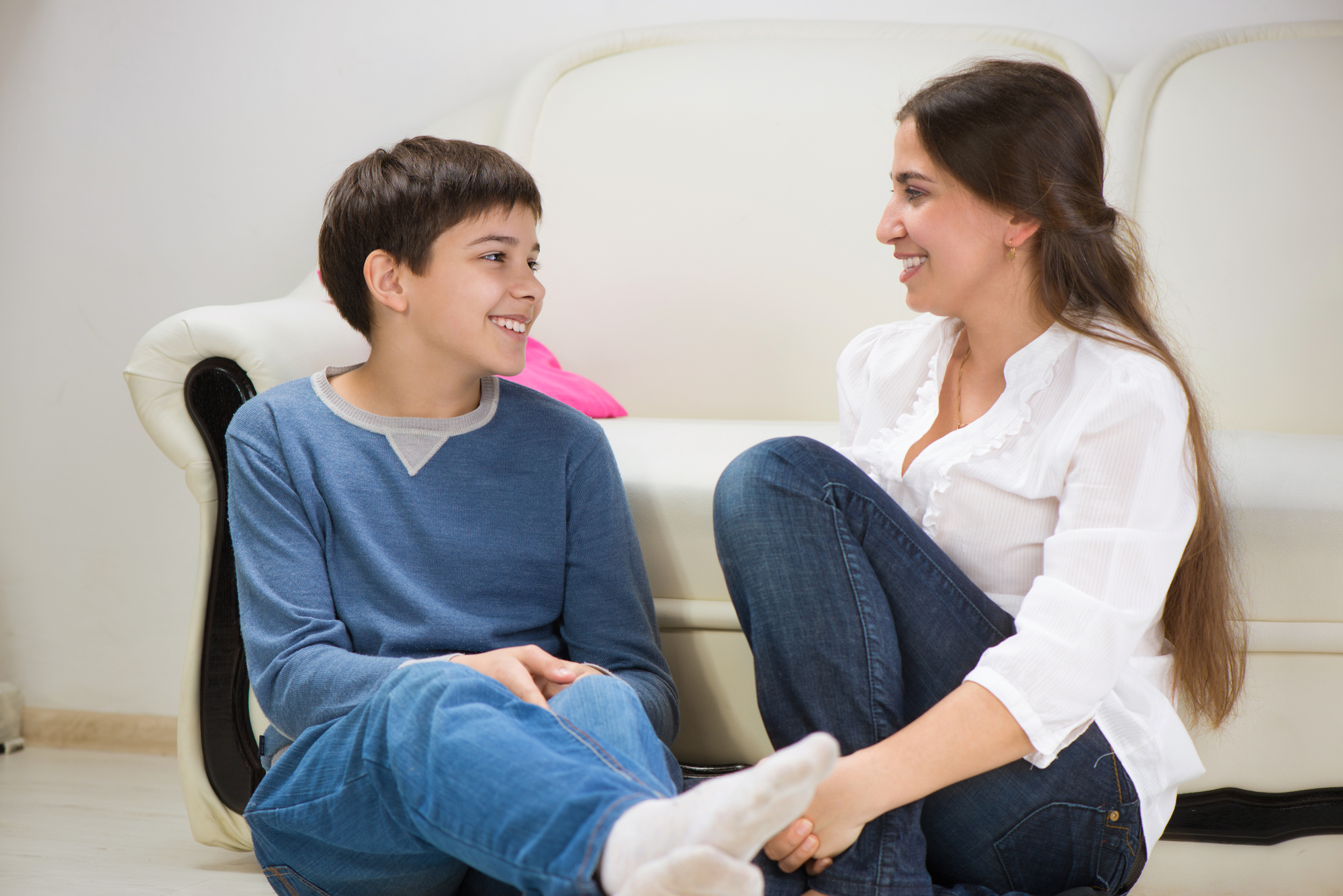 Son and mother sit on the floor in front of a white couch chatting